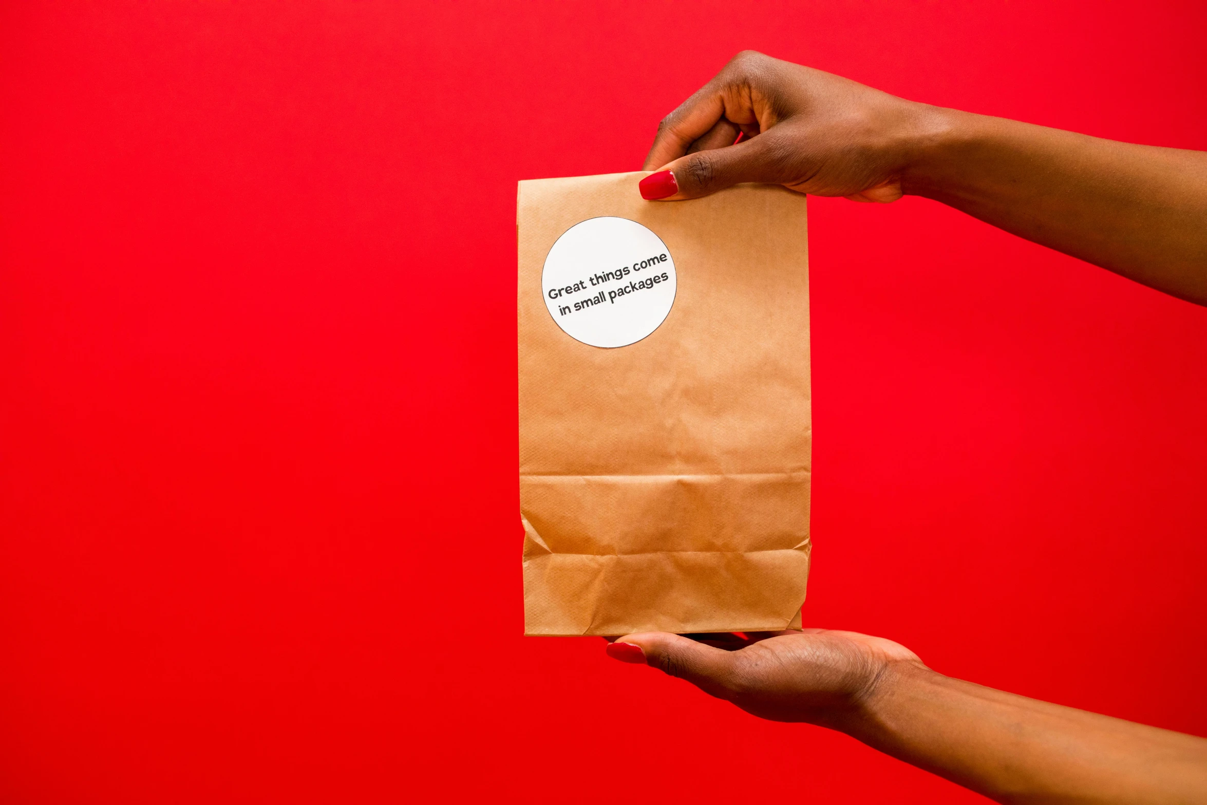 a person holding a brown paper bag with a sticker on it, private press, on a red background, serving suggestion, back towards camera, everything enclosed in a circle