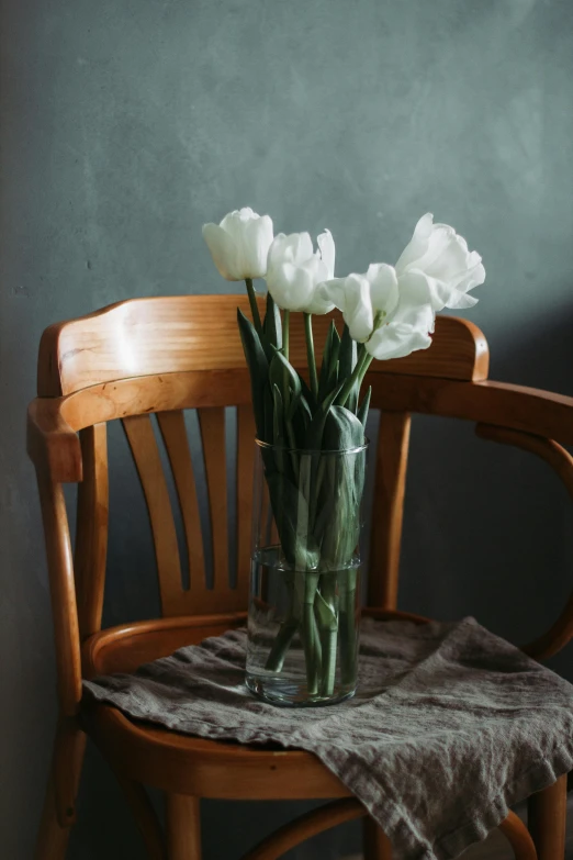 a vase filled with white flowers sitting on top of a wooden chair, a still life, inspired by Constantin Hansen, trending on unsplash, tulips, cozy arm chairs, sad scene, large tall