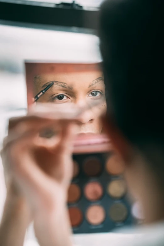 a close up of a person looking in a mirror, wearing eye shadow, looking at camera, looking down on the camera, medium-shot