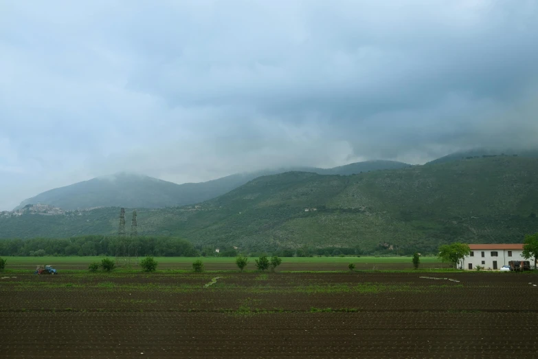 a field with a house and mountains in the background, by Muggur, dau-al-set, overcast lighting, journalism photo, photorealist, green