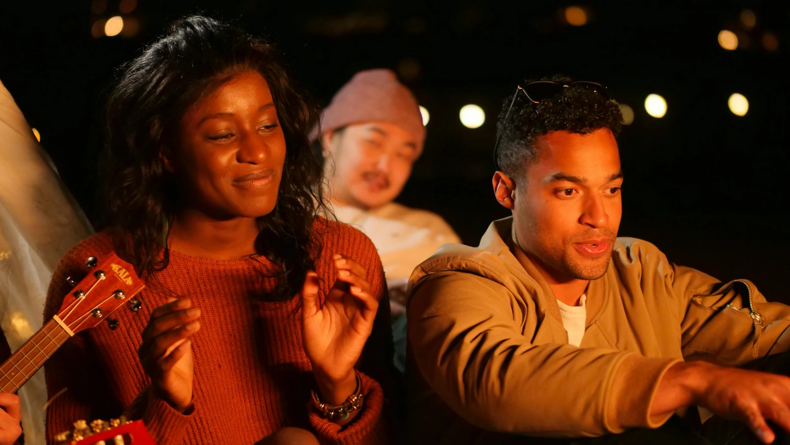 a man sitting next to a woman holding a guitar, at night time, 3 actors on stage, essence, bonfire