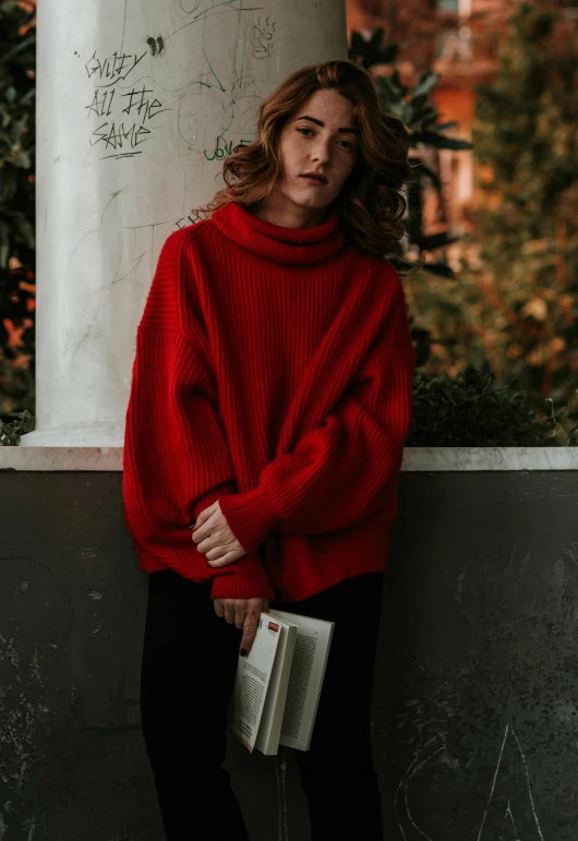 a woman in a red sweater leaning against a column, unsplash contest winner, holding books, style of julia razumova, with soft bushes, wearing turtleneck