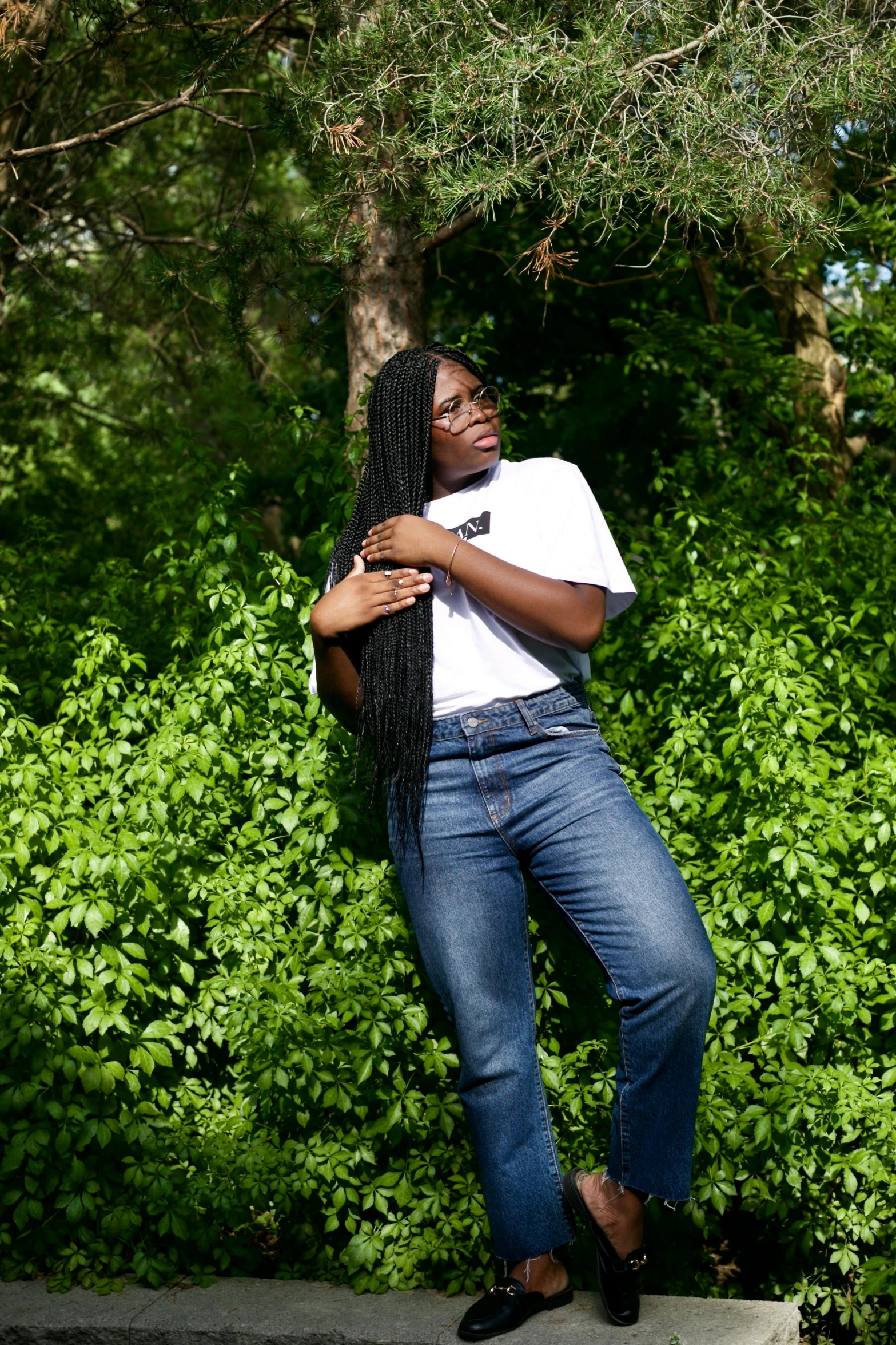 a woman with long black hair leaning against a tree, by Dulah Marie Evans, pexels contest winner, jeans and t shirt, african canadian, triumphant pose, greenery