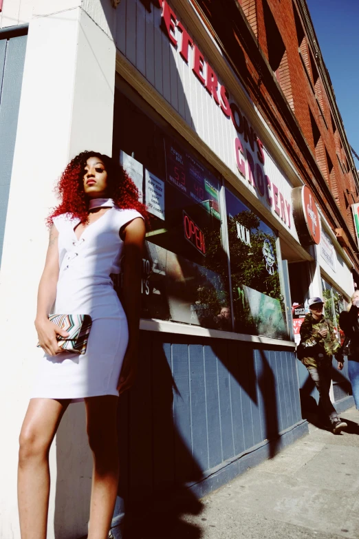 a woman in a white dress standing in front of a store, a photo, by Douglas Shuler, unsplash, doja cat, with red hair, teenage vanessa morgan, intense sunlight