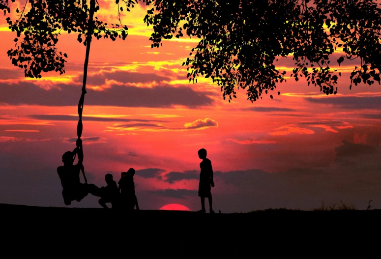 a group of people that are sitting on a swing, by Peter Churcher, pexels contest winner, redpink sunset, kids playing, hanging from a tree, sunset panorama