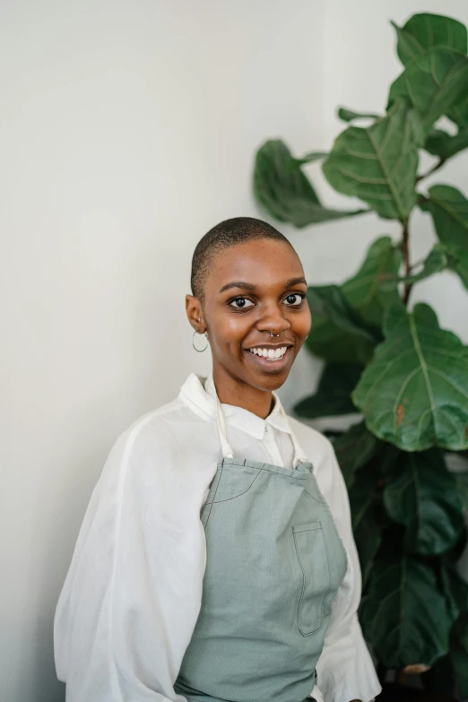 a woman standing in front of a potted plant, by Dulah Marie Evans, wearing an apron, short green bobcut, happy chef, dark natural glow