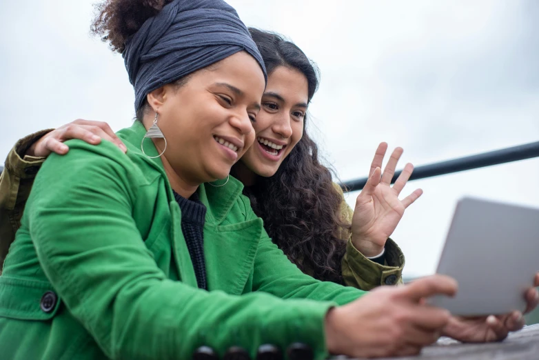 a couple of women sitting next to each other on a laptop, a picture, trending on pexels, waving and smiling, aida muluneh, on a bridge, full frame image