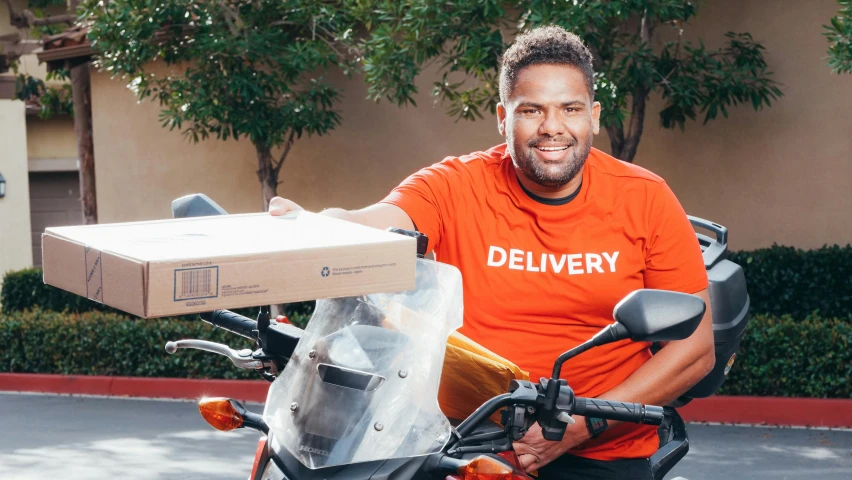 a man sitting on a motorcycle holding a box, profile image, brown skin man with a giant grin, thumbnail, darren bartley