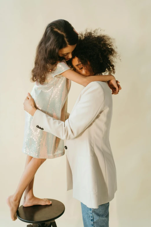 a woman standing next to a little girl on a stool, by Matija Jama, pexels, modernism, wearing silver silk robe, hugging each other, neutral colours, wearing disco suit