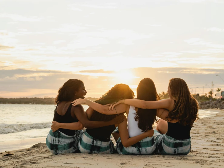 a group of women sitting on top of a sandy beach, pexels contest winner, her back is to us, sunset beach, brunettes, cuddling