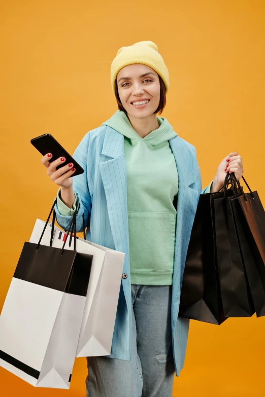 a woman holding shopping bags and a cell phone, a colorized photo, trending on pexels, wearing a yellow hoodie, 🚀🌈🤩, baggy clothing and hat, tech robes