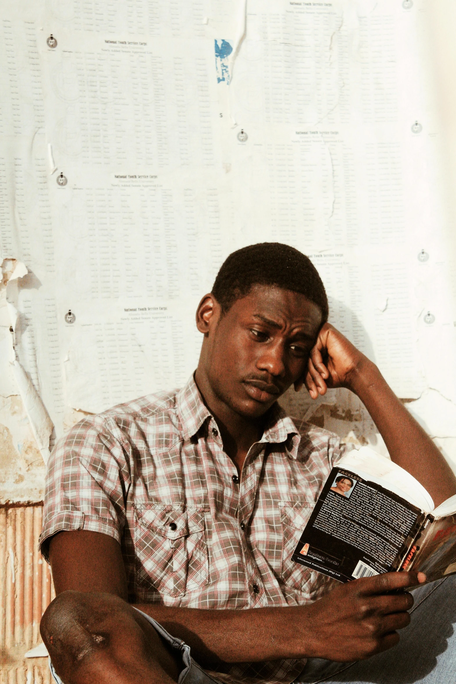 a man sitting on a bed reading a book, an album cover, by Robert Feke, ghanaian movie poster, holding notebook, concerned expression, 1 9 8 5 photograph