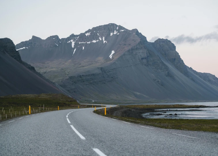 a road next to a body of water with mountains in the background, by Hallsteinn Sigurðsson, pexels contest winner, hurufiyya, very asphalt, sharp thick lines, peaks, youtube thumbnail