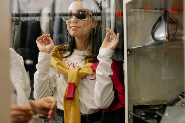 a woman that is standing in front of a mirror, sunglasses and a scarf, people shopping, inside a glass box, gen z