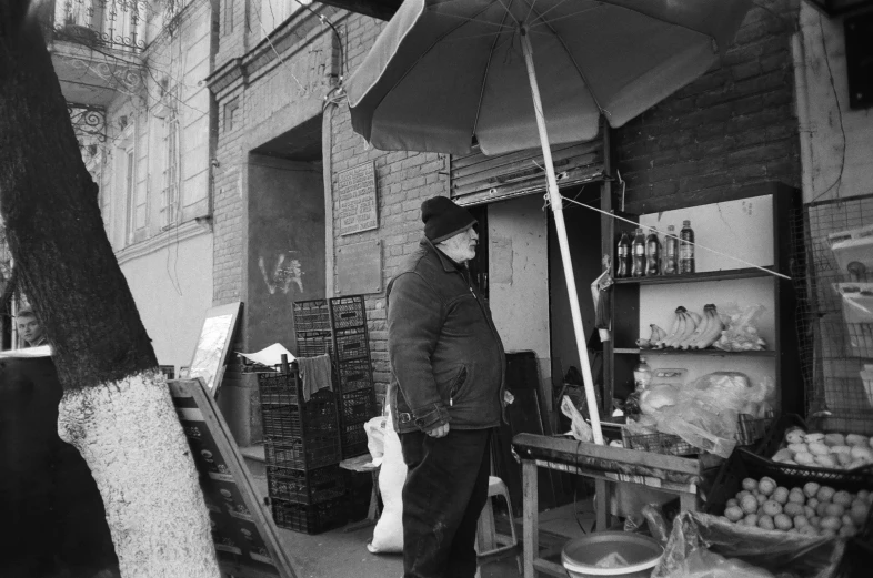 a black and white photo of a man standing under an umbrella, a black and white photo, street vendors, azamat khairov, brooklyn, cold scene