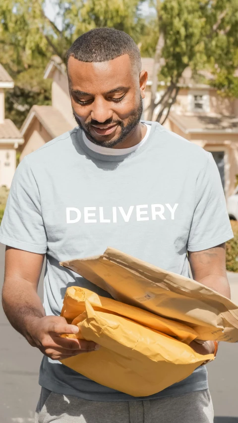 a man holding a package in front of a house, pexels contest winner, hurufiyya, graphic tees, grey, ( ( dark skin ) ), dynamic closeup