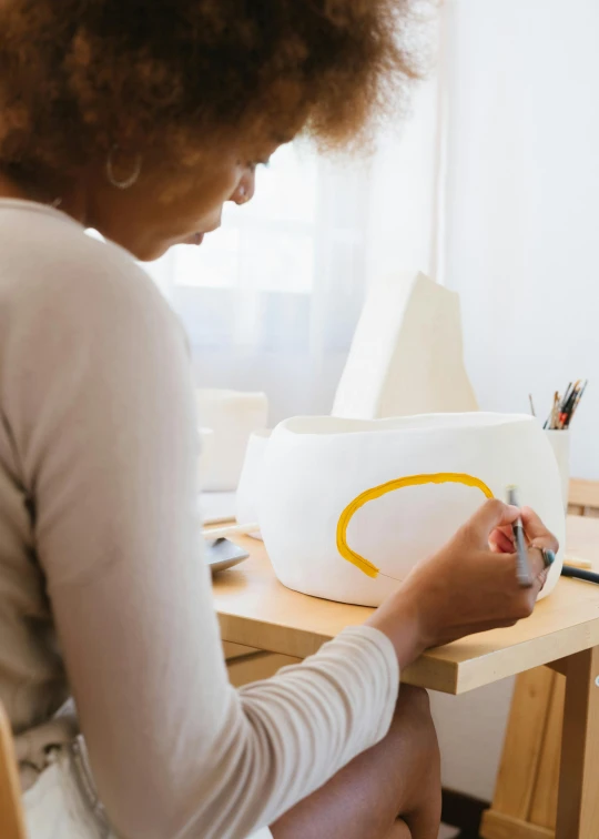 a woman sitting at a desk in front of a computer, an airbrush painting, inspired by Sarah Lucas, trending on unsplash, white ceramic shapes, white and yellow scheme, hand built ceramics, profile image