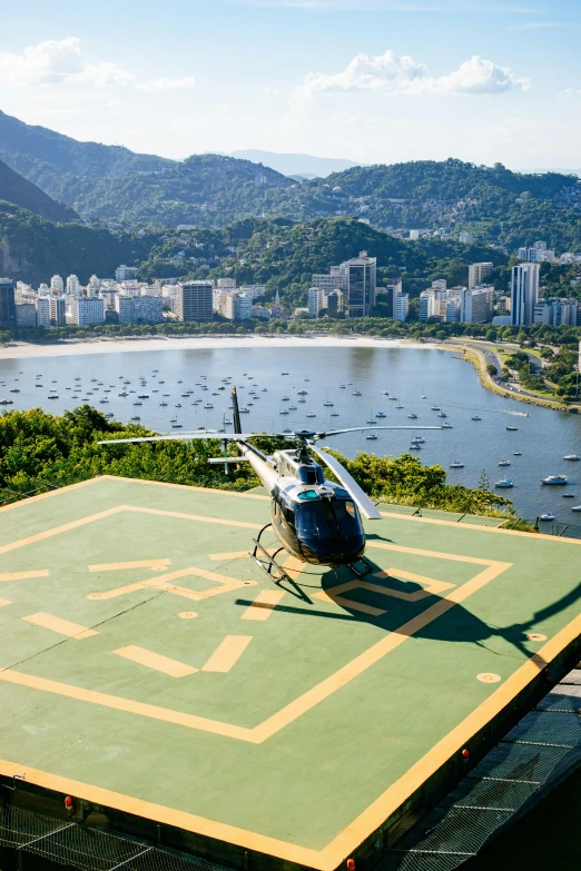 a helicopter sitting on top of a green field, by Felipe Seade, with a city in the background, on the ocean, sport, bl