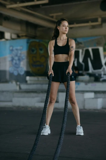 a woman holding a rope in a gym, by Emma Andijewska, tight black tank top and shorts, on rooftop, promo image, shot with sony alpha