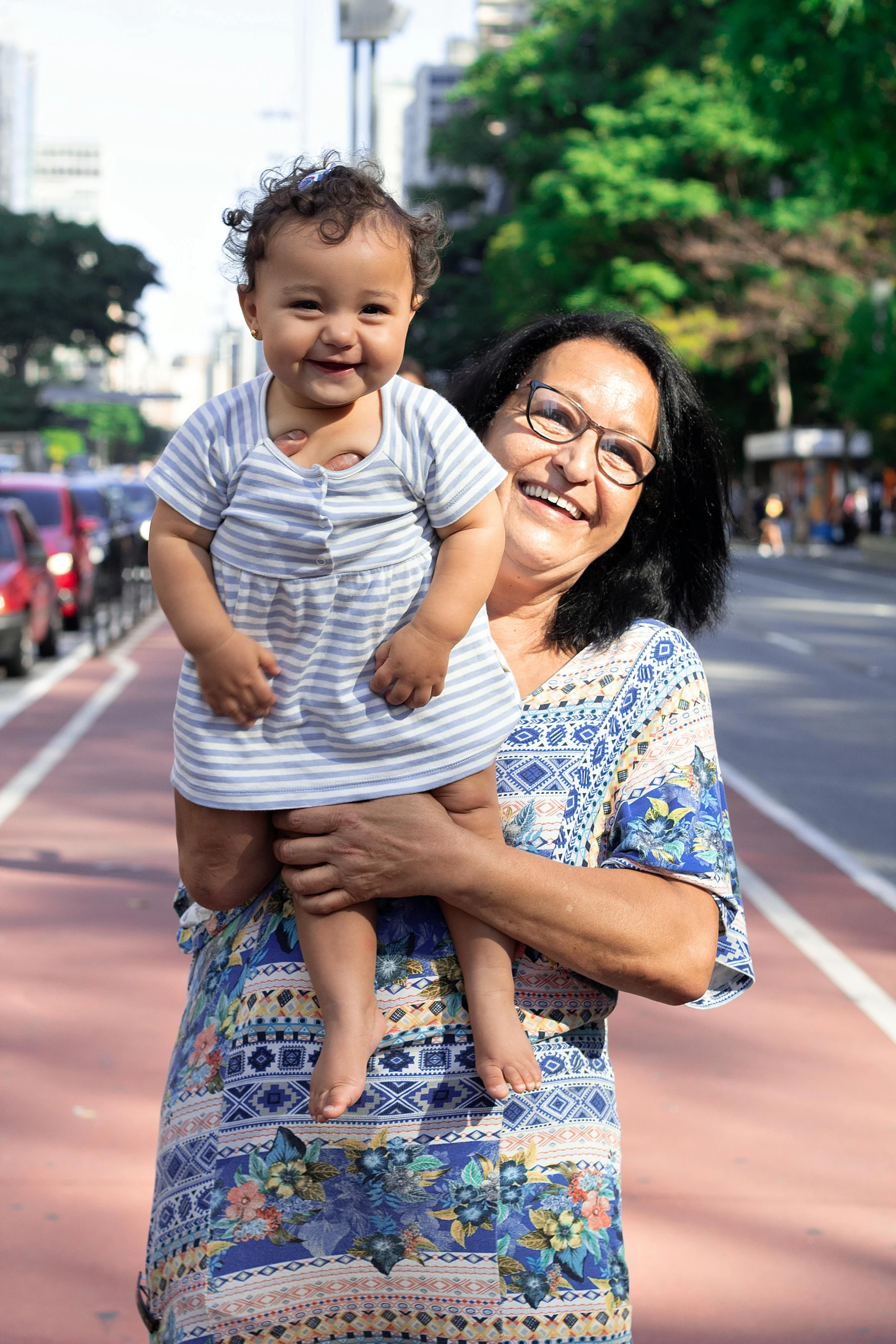 a woman holding a baby in her arms, by Judith Gutierrez, reddit, standing on street corner, jakarta, smiling, avatar image