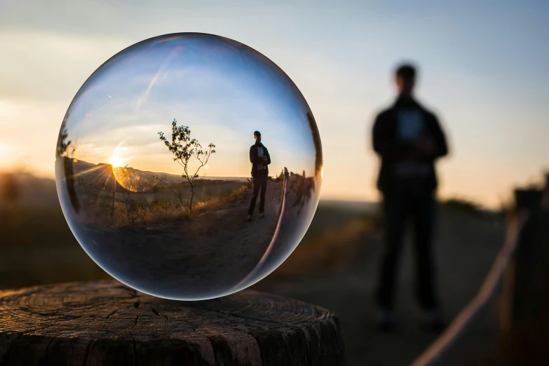 a glass ball sitting on top of a wooden post, by Jesper Knudsen, unsplash contest winner, hyperrealism, person in foreground, refracted sunset, ultrawide lens”, refractive crystal