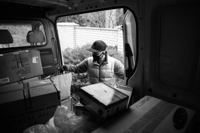 a man that is standing in the back of a van, a black and white photo, by Andrew Stevovich, pexels, arbeitsrat für kunst, delivering packages for amazon, 🌸 🌼 💮, people at work, jen yoon