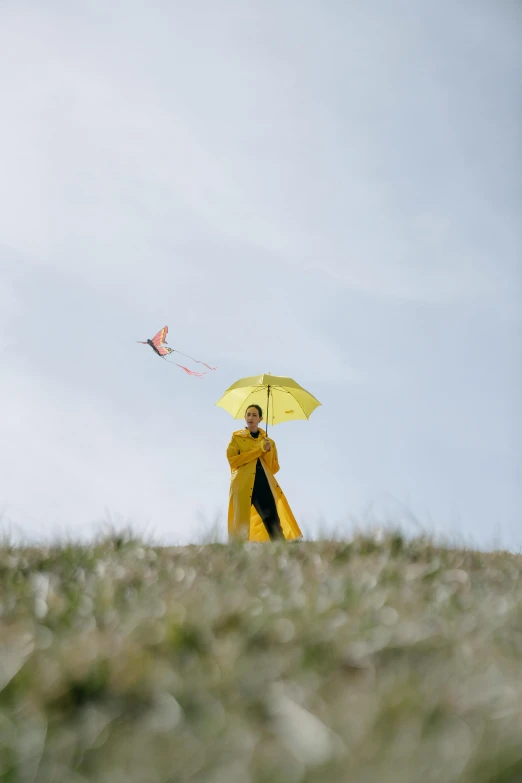 a woman in a yellow raincoat is flying a kite, inspired by Jan Rustem, unsplash, standing on a hill, monk, photographed for reuters, clown