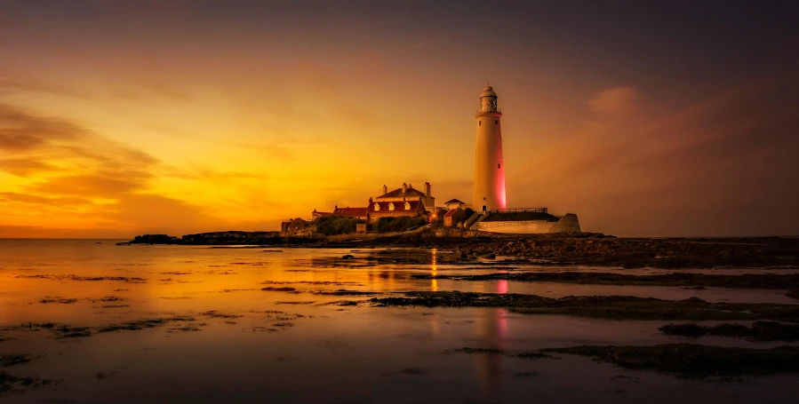 a lighthouse sitting on top of a sandy beach, by Lee Loughridge, pexels contest winner, romanticism, red and orange glow, yellow light, professionally post-processed, yorkshire