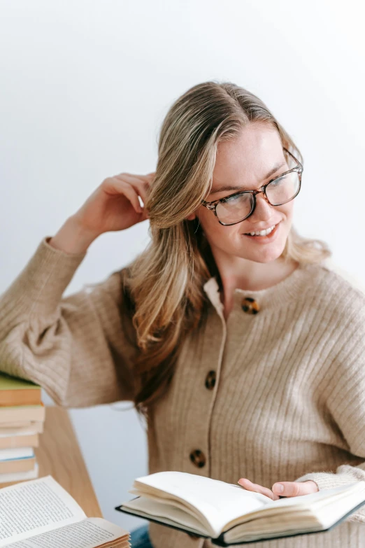 a woman sitting at a table reading a book, wearing a cardigan, half-frame square glasses, sydney sweeney, detailed product image