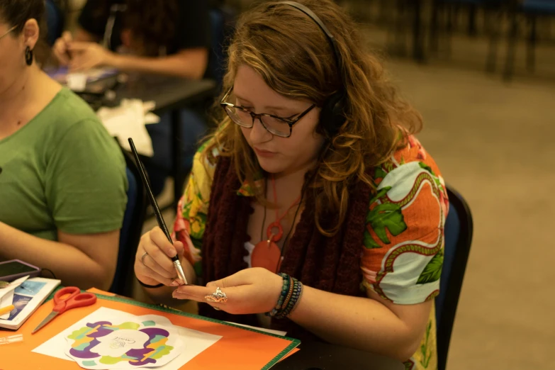 a couple of women that are sitting at a table, an airbrush painting, academic art, holding a paintbrush, tie-dye, tabletop gaming, student