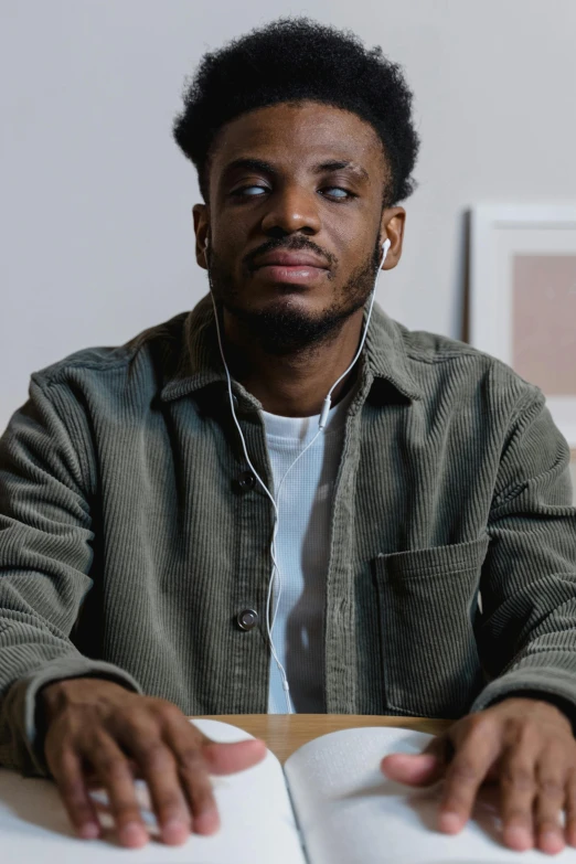 a man sitting at a table with an open book, an album cover, inspired by Willian Murai, trending on pexels, realism, confident smirk, ( ( dark skin ) ), twitch streamer / gamer ludwig, full frame image