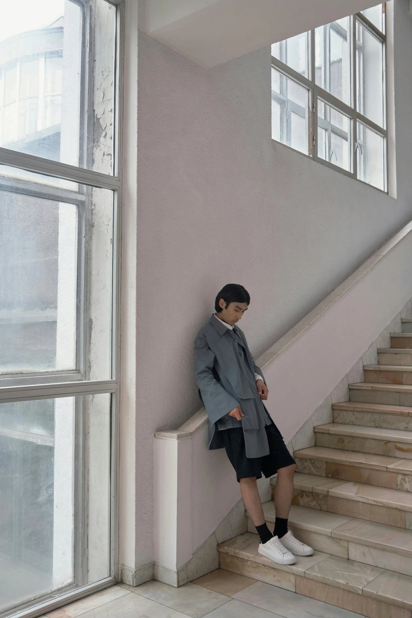 a man sitting on the stairs of a building, an album cover, inspired by Gao Xiang, unsplash, postminimalism, short skirt and a long jacket, blue gray, in a hotel hallway, bo xun ling