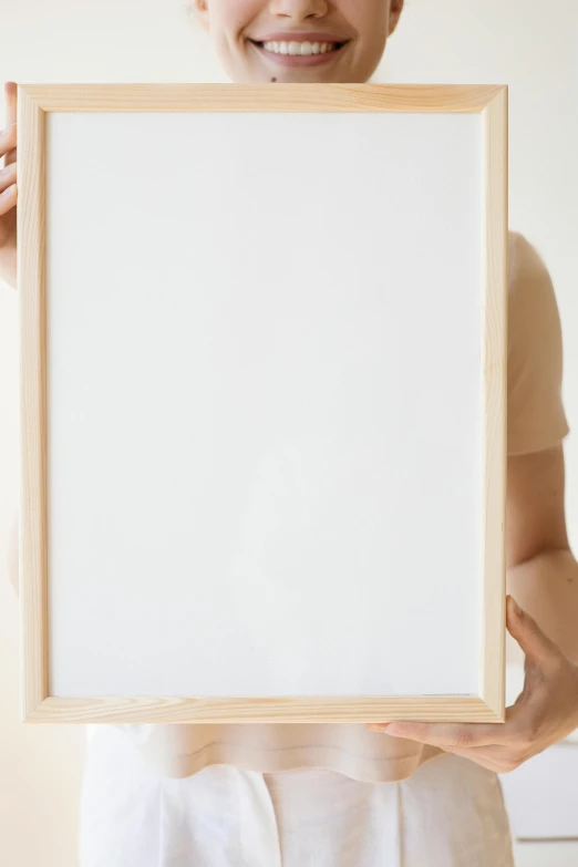 a woman holding a picture frame in front of her face, a poster, trending on unsplash, visual art, light cream and white colors, blank background, wooden frame, high-quality photo