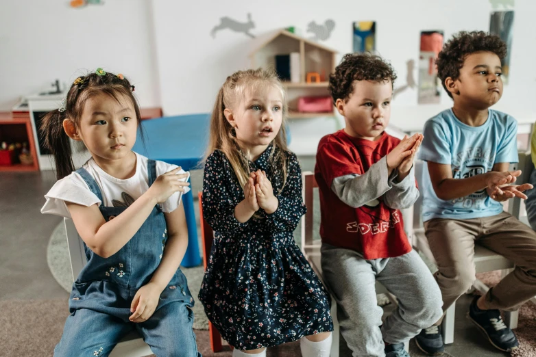 a group of children sitting next to each other, by Arabella Rankin, pexels contest winner, shrugging, doing a prayer, sitting in the classroom, toddler