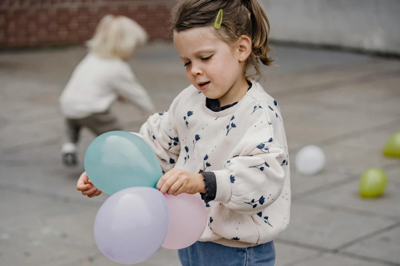 a little girl holding a bunch of balloons, by Emma Andijewska, pexels contest winner, interactive art, urban playground, wearing a cute top, soft cool colors, marbles