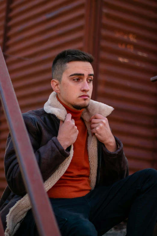 a man sitting on the steps of a building, a colorized photo, trending on pexels, leather fur jacket, ((rust)), hasan piker, non-binary