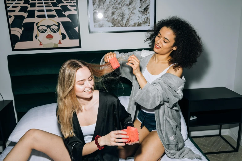 a couple of women sitting on top of a bed, trending on unsplash, happening, styled hair, holding a stuff, full product shot, bowater charlie and brom gerald