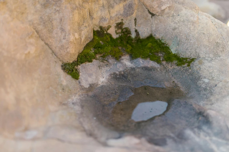 a small pool of water sitting on top of a rock, unsplash, land art, roman bath, detail shot, craggy, mold