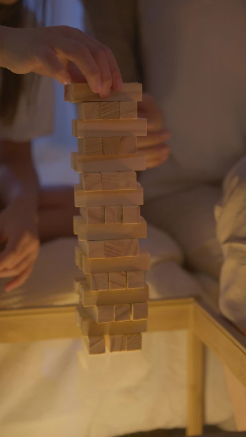 a group of people playing a game of wooden blocks, an album cover, inspired by Isamu Noguchi, unsplash, soft lighting 8k, in the bedroom at a sleepover, colossal tower, shot on sony a 7