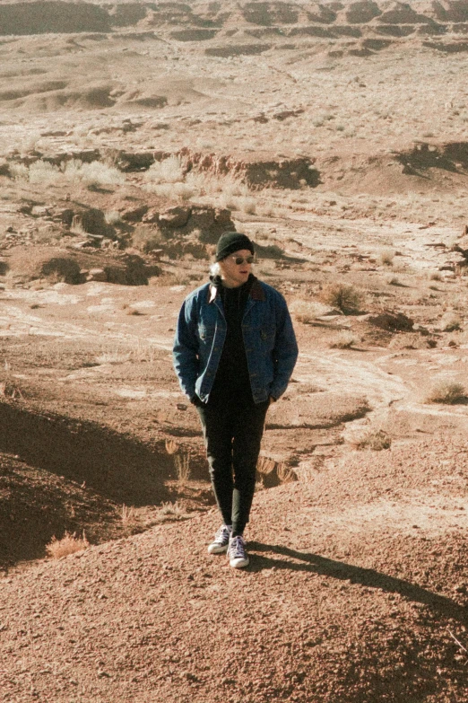 a man standing in the middle of a desert, an album cover, by Robbie Trevino, wearing jeans and a black hoodie, non-binary, wearing blue jacket, wearing sunglasses and a cap