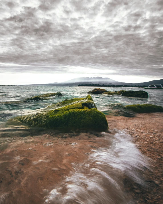 a large body of water sitting on top of a sandy beach, mossy stone, gloomy skies, in the sea, 500px photos