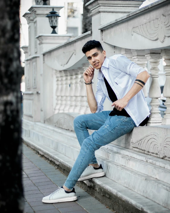 a man sitting on a ledge next to a tree, inspired by Randy Vargas, pexels contest winner, renaissance, outfit : jeans and white vest, non binary model, freddy mamani silvestre facade, asher duran