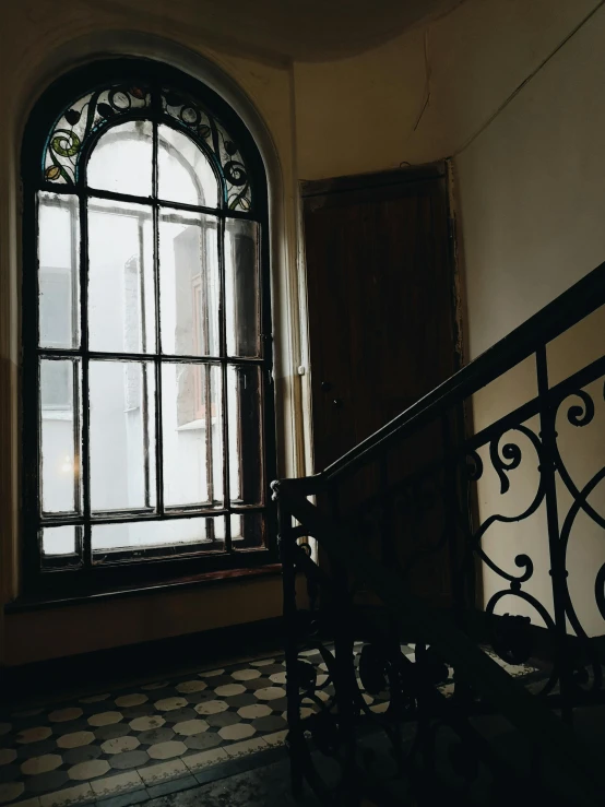 a black and white photo of a window in a building, inspired by Elsa Bleda, unsplash contest winner, stairs and arches, in a dusty victorian home, stained glass windows, apartment hallway