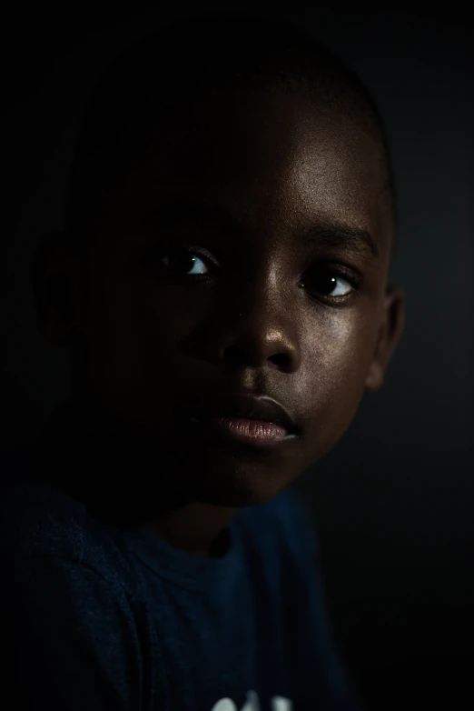 a close up of a child's face in the dark, an album cover, inspired by Gordon Parks, visual art, dramatic lowkey studio lighting, ( ( dark skin ) ), hes alone, underexposed grey