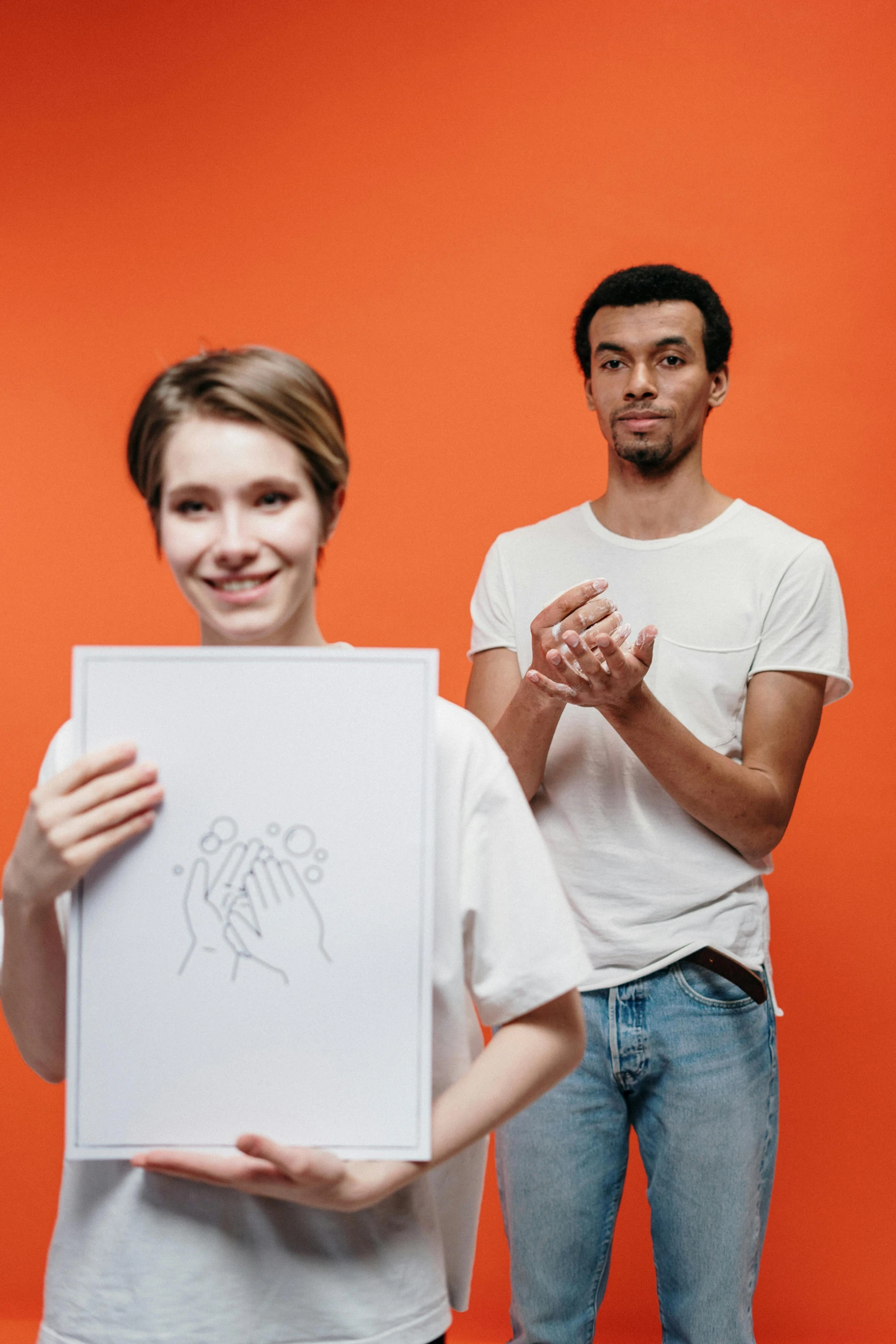 a man and a woman holding up a piece of paper, an album cover, pexels contest winner, visual art, orange and white, gesture drawn, non binary model, yulia nevskaya