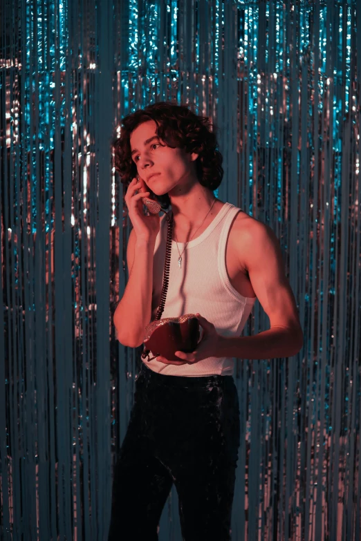 a man standing in front of a curtain talking on a cell phone, an album cover, inspired by Nan Goldin, pexels, magic realism, robert sheehan, cute young man, sparkly, holding maracas