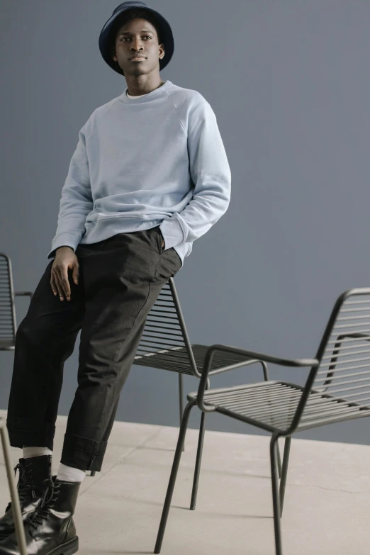 a man sitting on top of a metal chair, inspired by Constantin Hansen, trending on unsplash, photorealism, pale blue outfit, wearing sweatshirt, grey pants and black dress shoes, with two front pockets