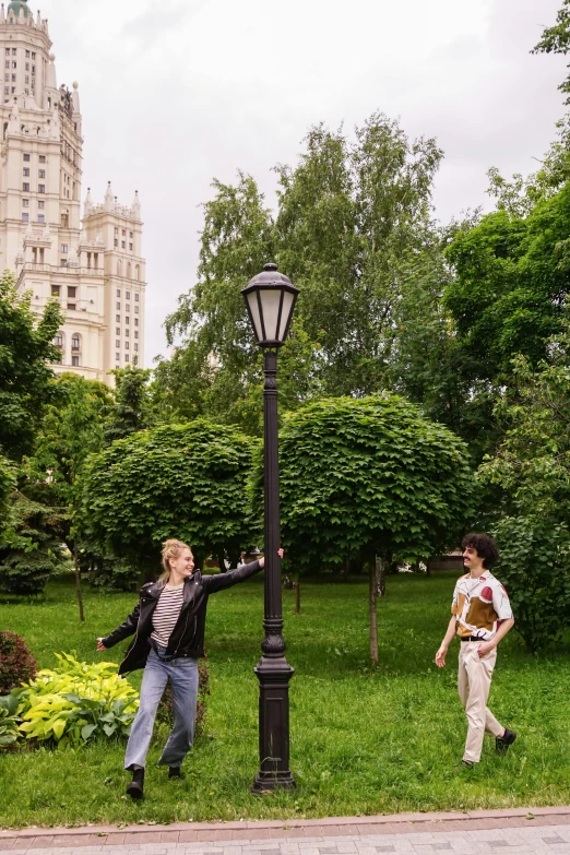 a couple of people that are standing in the grass, by Serhii Vasylkivsky, unsplash, socialist realism, big beautiful street lamps, square, lush garden surroundings, in moscow centre