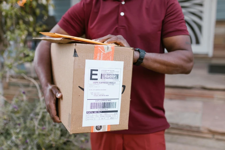 a man in a red shirt holding a box, pexels contest winner, emmanuel shiru, delivering mail, avatar image, close up image