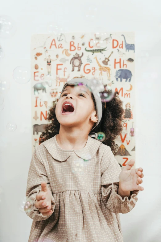 a little girl that is standing in front of a wall, art & language, bubbles in the air, smiling down from above, wholesome, official product photo